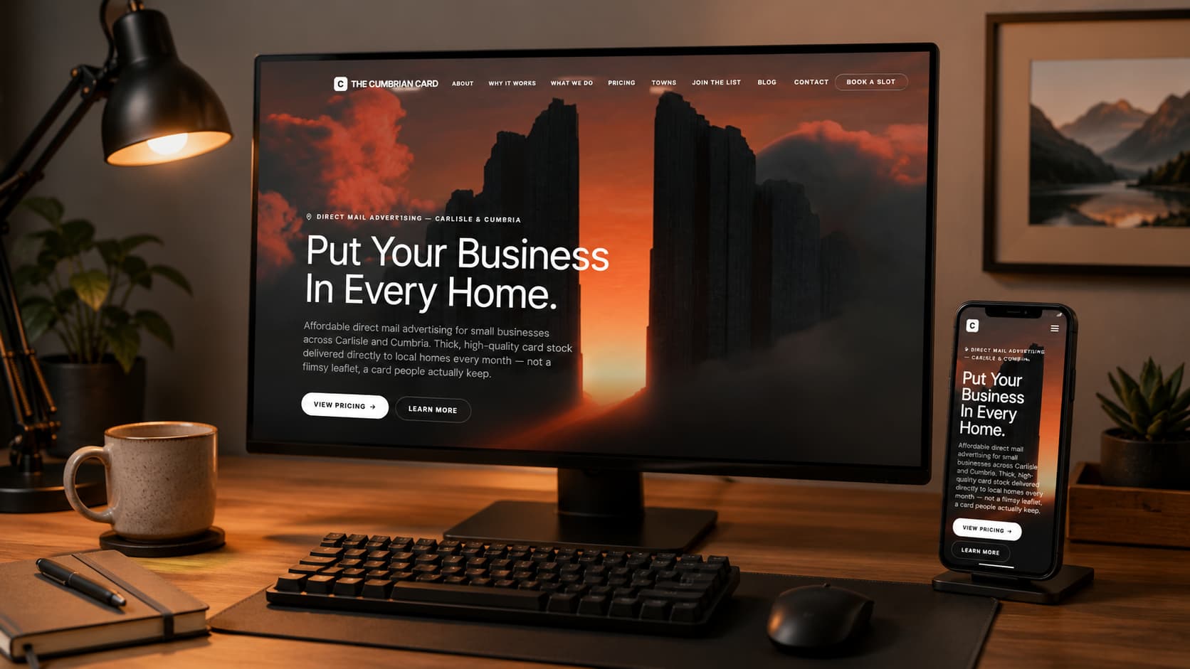 The Cumbrian Card website shown on a desktop monitor and phone in a home office